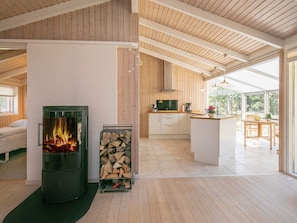 A modern interior with a wood-burning stove, a kitchen area, and a dining space with a view. - Holiday Home in Strandby (Strandby)