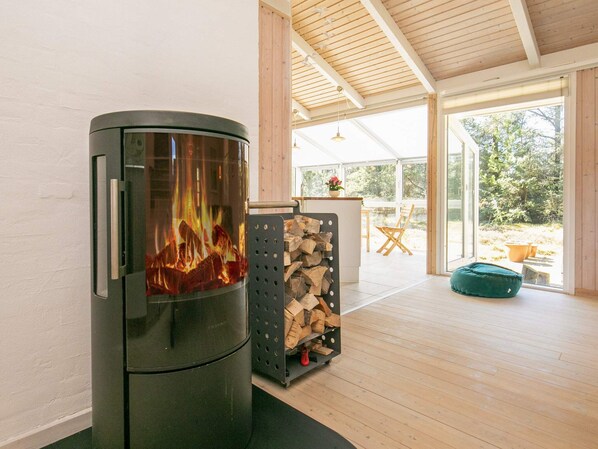 A modern interior with a wood-burning stove, a stack of firewood, and a view of the outdoors.