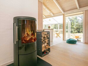 A modern interior with a wood-burning stove, a stack of firewood, and a view of the outdoors.
