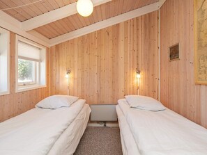 A room with two single beds, wooden panel walls, a window with blinds, and a ceiling light fixture. - Holiday Home in Strandby (Strandby)