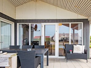 Eine Terrasse im Freien mit Tisch, Stühlen, einer Bank und einer Glastür, die zu einem überdachten Bereich führt.