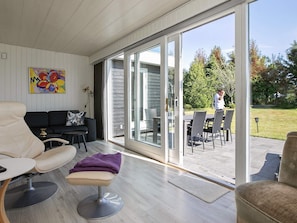 A modern interior with a sofa, a chair, and a dining area with a table and chairs. - Holiday Home in Væggerløse (Vaeggerlose)