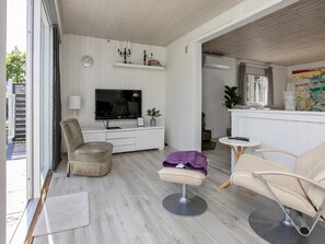 A modern living room with a flat-screen TV, a sofa, a chair, and a small table. - Holiday Home in Væggerløse (Vaeggerlose)