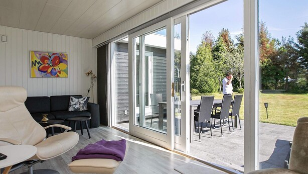 A modern living room with a sofa, a chair, and a dining area with a table and chairs. - Holiday Home in VÃ¦ggerlÃ¸se (Vaeggerlose)