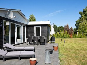 A modern outdoor patio with a dining set, lounge chairs, and a barbecue grill. - Holiday Home in Væggerløse (Vaeggerlose)