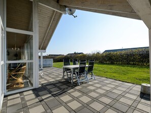 Une terrasse couverte avec une table et des chaises, donnant sur un jardin, et une antenne parabolique.