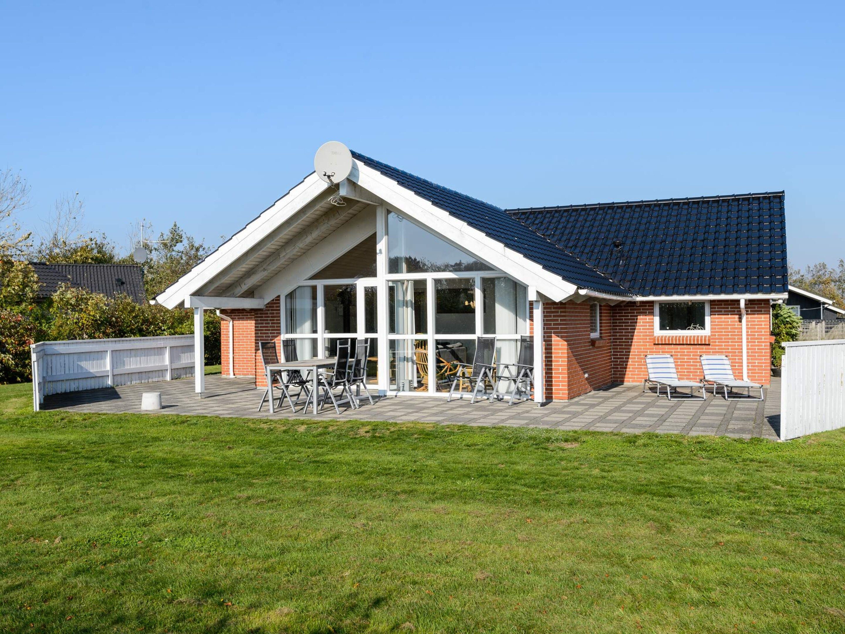 Une maison avec un toit en pente, de grandes fenêtres et un patio aménagé avec du mobilier d’extérieur.