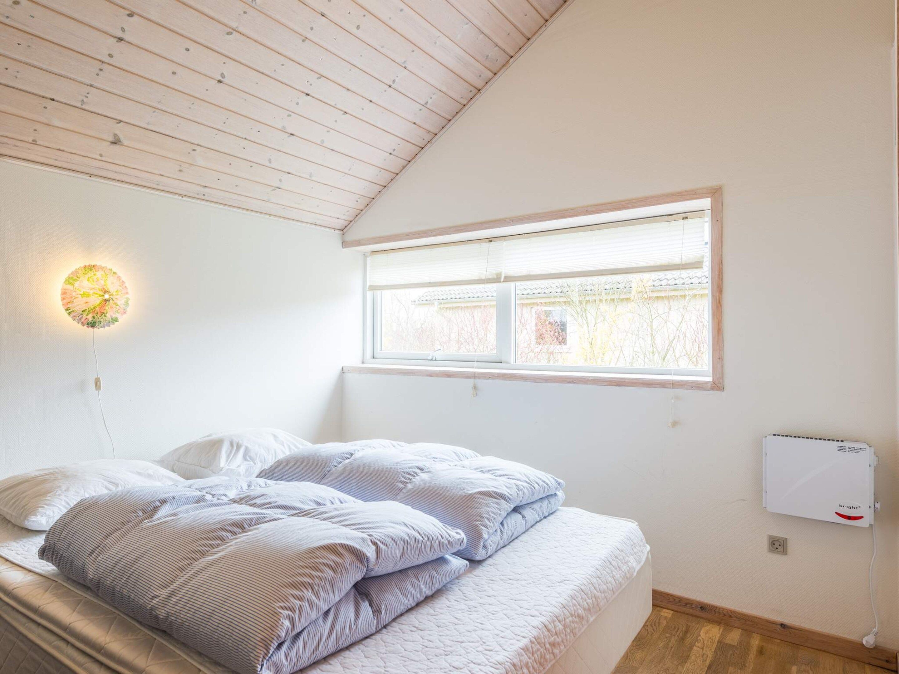 A bedroom with a bed, a wall-mounted light fixture, a window, and a power outlet.