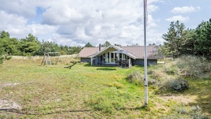 A house with a sloped roof, a porch with outdoor seating, and a tall flagpole in front. - Charming Cottage Retreat-by Traum (Blavand)