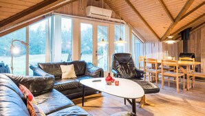 A spacious living area with a large black leather sofa, a white coffee table, and a dining table with chairs. - Charming Cottage Retreat-by Traum (Blavand)