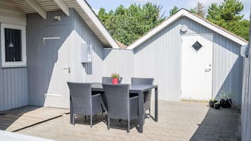 A covered patio area with a table and chairs, a small garden, and a shed in the background.