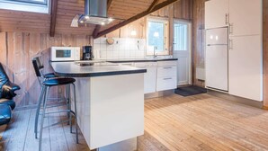 A modern kitchen with wooden walls, a central island, bar stools, and a built-in microwave. - Charming Cottage Retreat-by Traum (Blavand)