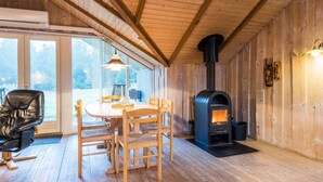 A cozy wooden interior with a dining area, a black stove, and large windows. - Charming Cottage Retreat-by Traum (Blavand)