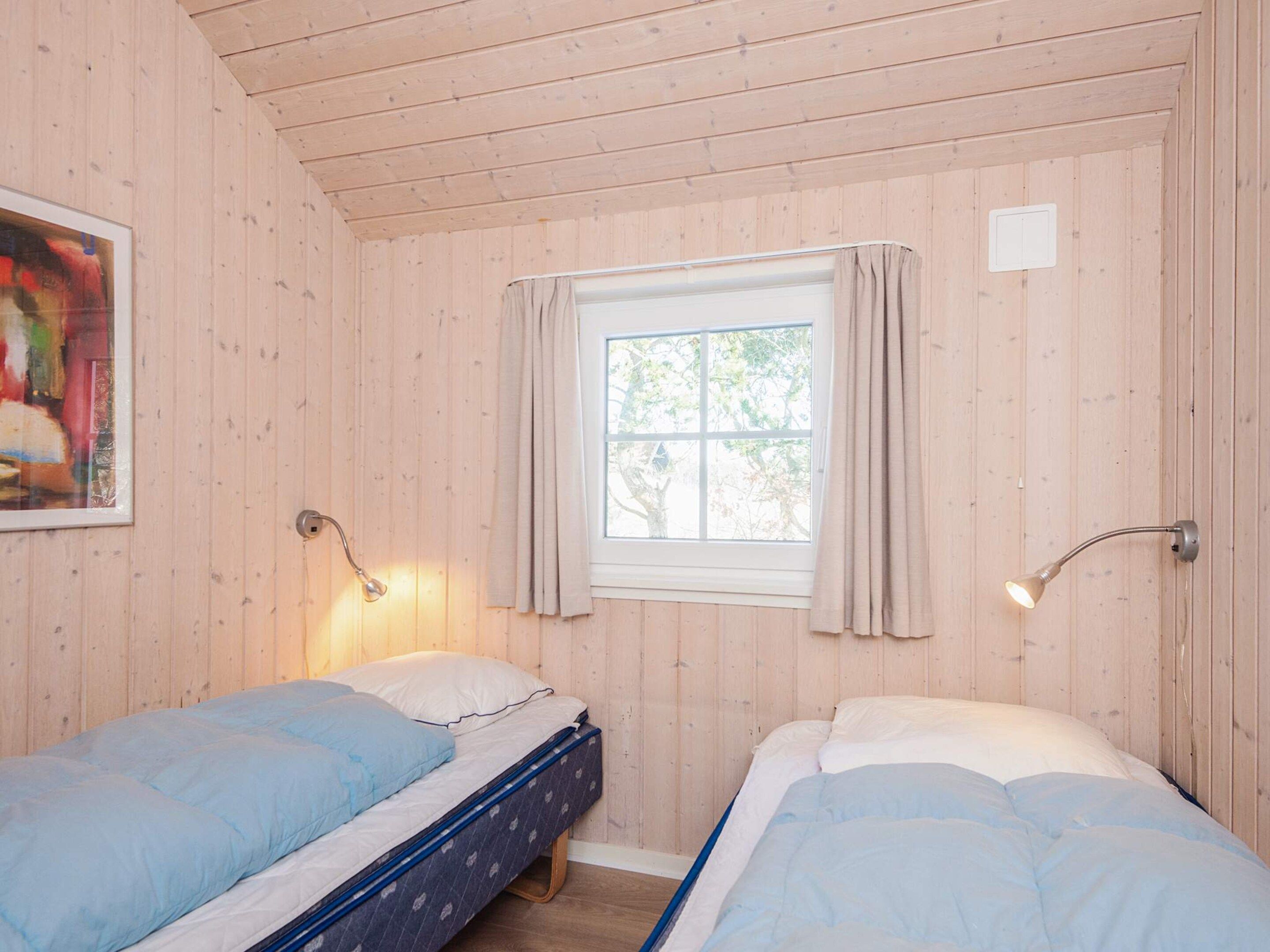 Quarto com duas camas, janela com cortinas, luminária na parede e um quadro.