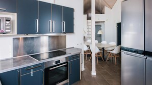 A modern kitchen with stainless steel appliances, dark blue cabinets, and a dining area with white chairs. - 5 Star Holiday Home in Blavand (Blavand)