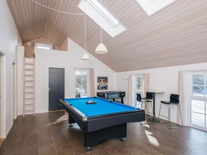 Een ruime kamer met een pooltafel, een tafelvoetbaltafel en een zithoek met een tafel en stoelen.