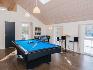 A pool table with a foosball table and chairs in a room with large windows and a high ceiling.