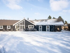 Un bâtiment doté d’une grande entrée avec une porte en verre, d’un espace extérieur abrité avec des sièges et d’un sol recouvert de neige.