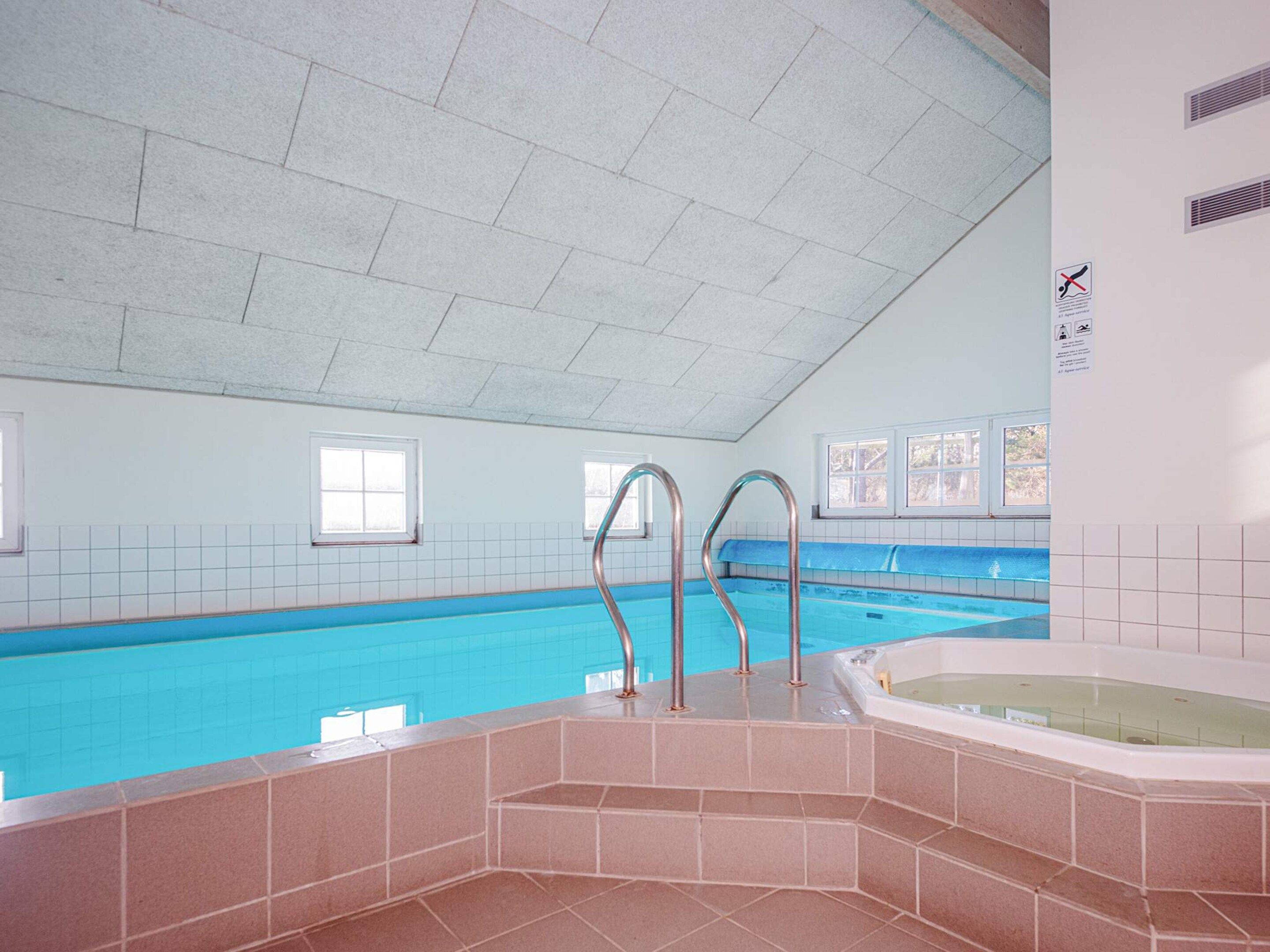 En indendørs swimmingpool med krystalklart vand, et jacuzzi og flisebeklædte vægge.