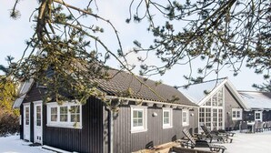A wooden cabin with a sloped roof, a small deck, and a fire pit area. - 5 Star Holiday Home in Blavand (Blavand)