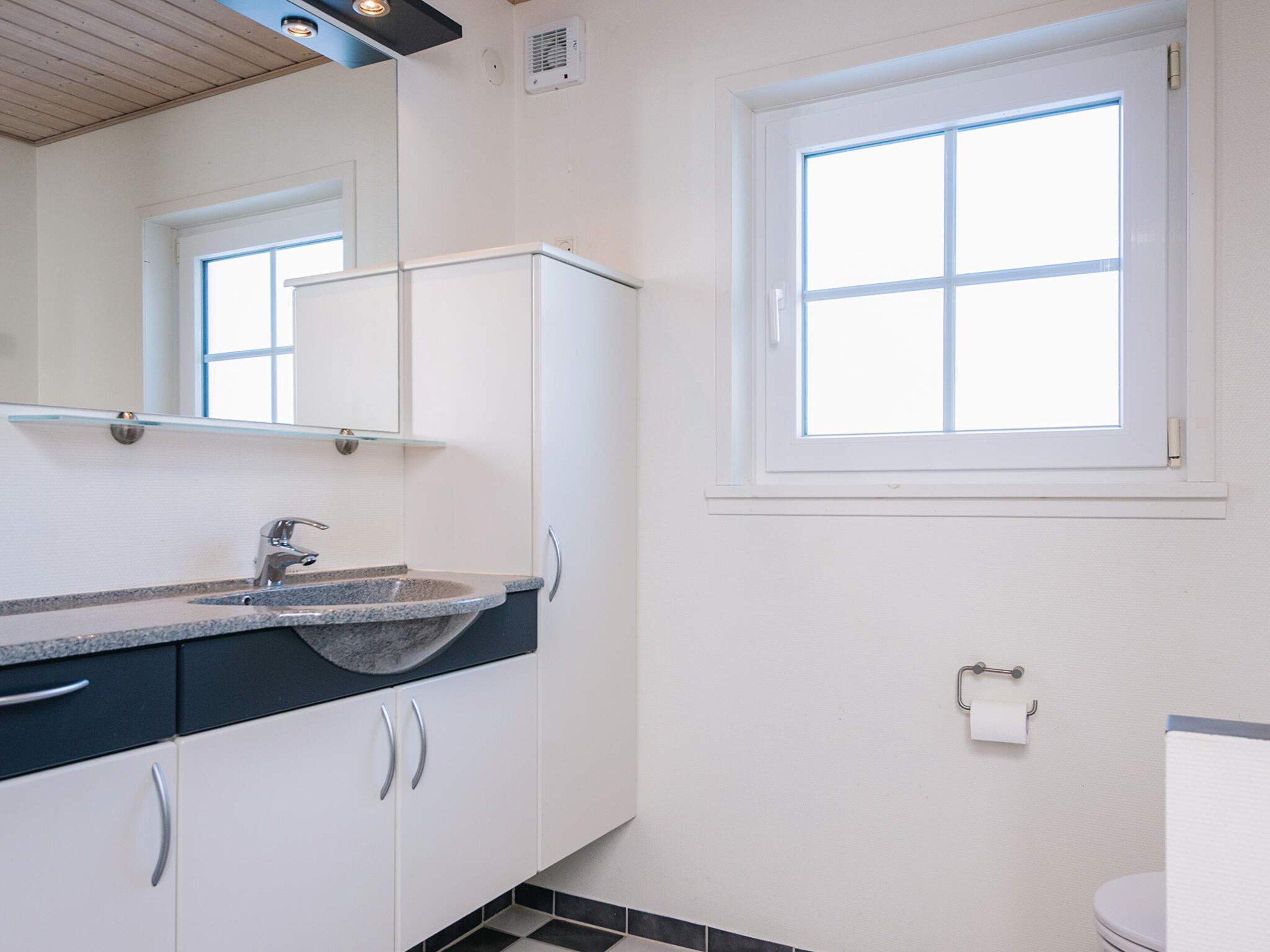 Une salle de bain comprenant un lavabo, un miroir, des placards, une fenêtre et des toilettes.