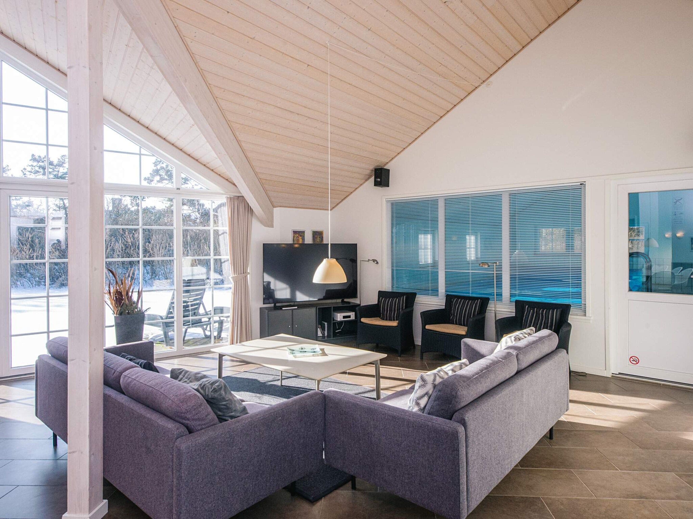 Un salon moderne avec un canapé, une table basse et des fauteuils. On y trouve également un téléviseur et une fenêtre avec des stores.