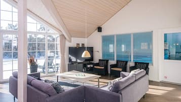 A modern living room with a sofa, coffee table, and chairs. There is a television and a window with blinds.