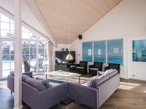 A modern living room with a sofa, coffee table, and chairs. There is a television and a window with blinds. - 5 Star Holiday Home in Blavand (Blavand)
