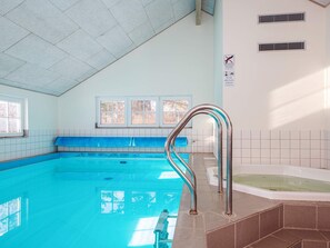 Une piscine intérieure avec un sol carrelé de bleu, un escalier métallique et un espace dédié à un jacuzzi.