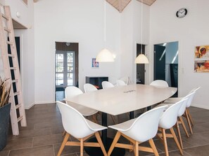 A modern dining area with a large table, white chairs, and pendant lighting.