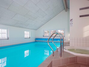 Une piscine intérieure à l’eau d’un bleu limpide, avec un escalier en métal et un jacuzzi.