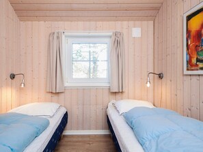 A room with two beds, a window with curtains, and wall-mounted lamps.