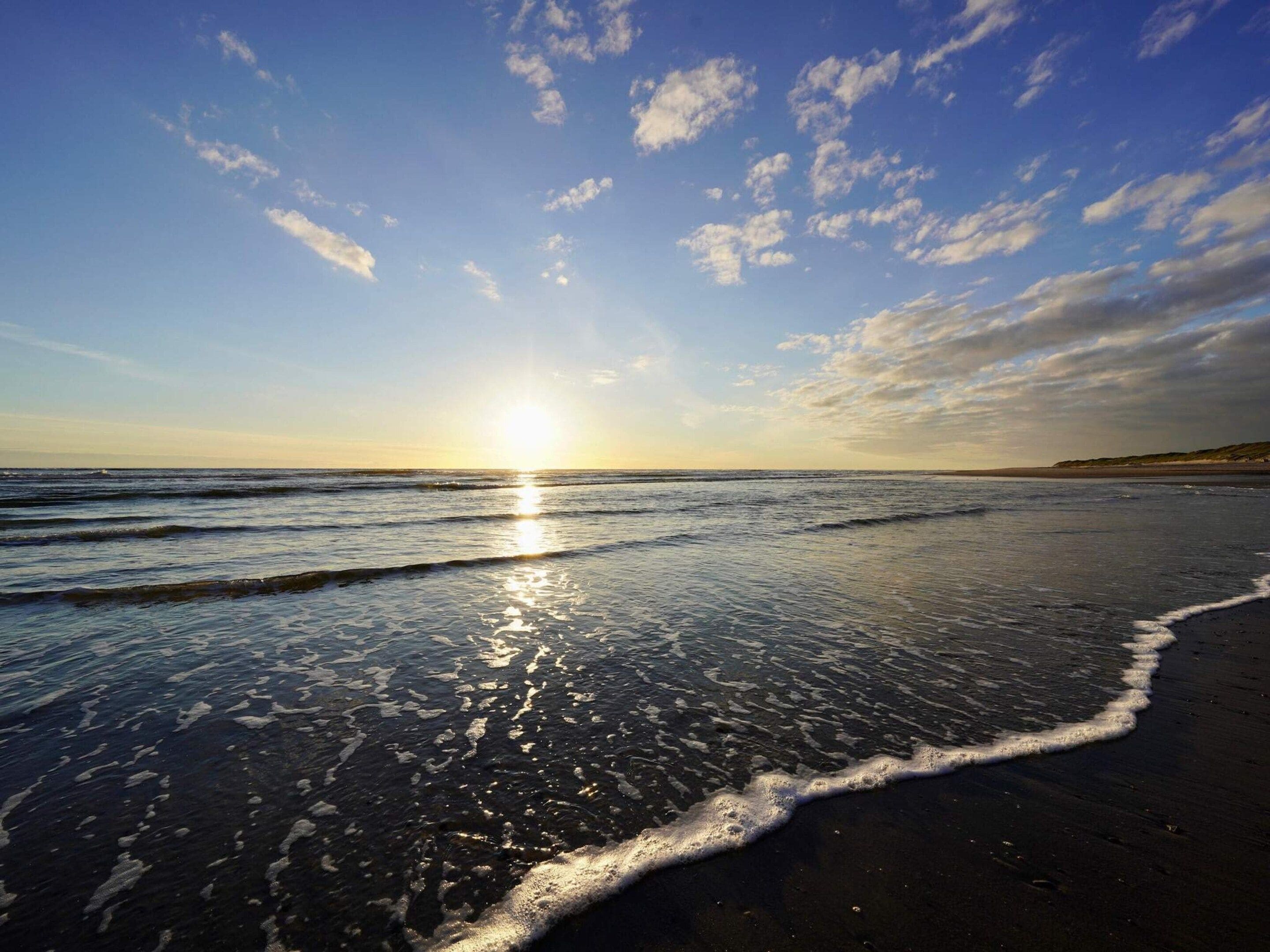 Une plage avec des vagues, un ciel dégagé et le soleil se couchant ou se levant.