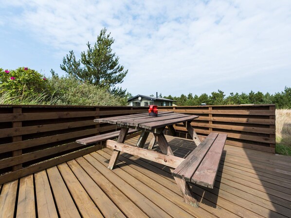 A wooden deck with a picnic table and benches, surrounded by a wooden fence and vegetation.