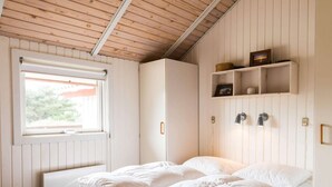 Een slaapkamer met een bed, een raam, een kledingkast en een plank met decoratieve spullen.