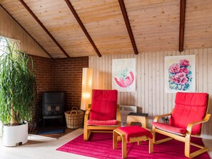 A cozy room with a fireplace, two red chairs, a large potted plant, and two wall-mounted paintings.