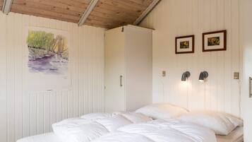 Une chambre avec un plafond en bois, des murs blancs, un lit avec une literie blanche et deux tableaux encadrés accrochés au mur.