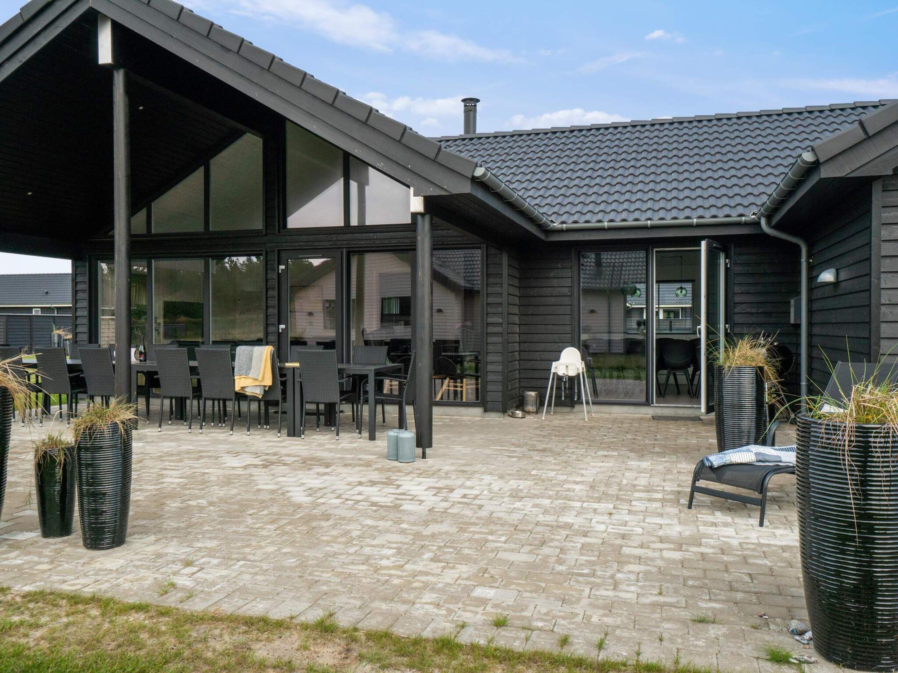 A modern outdoor patio with a brick floor, black furniture, and potted plants.