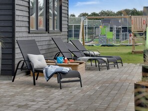 A patio with outdoor lounge chairs and a wooden table with cushions and a blanket.