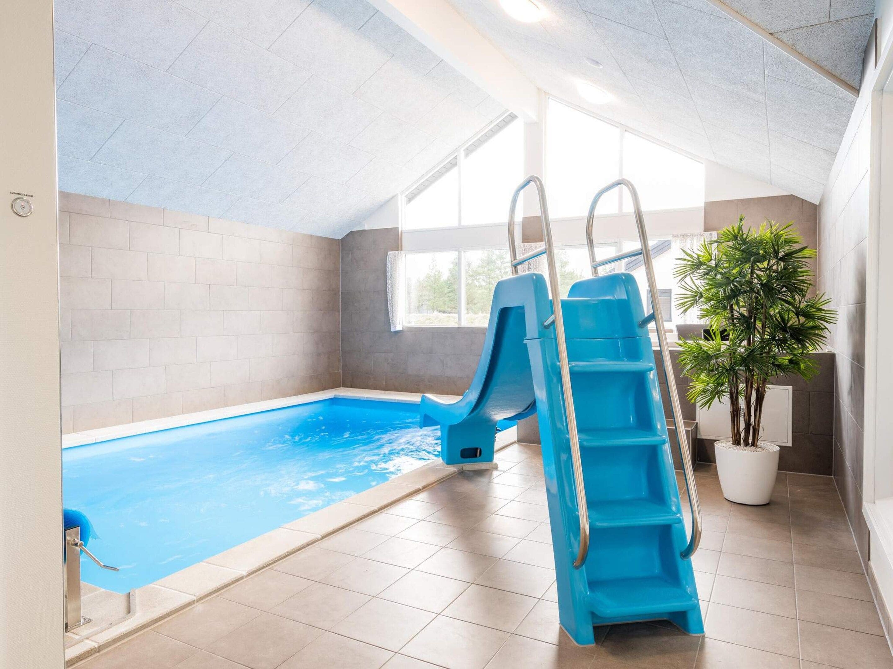 Una piscina interior con tobogán, una planta en maceta y un ventanal que proporciona luz natural.