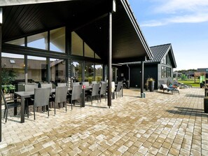 An outdoor patio area with tables and chairs, a covered seating area, and a view of a building in the background.