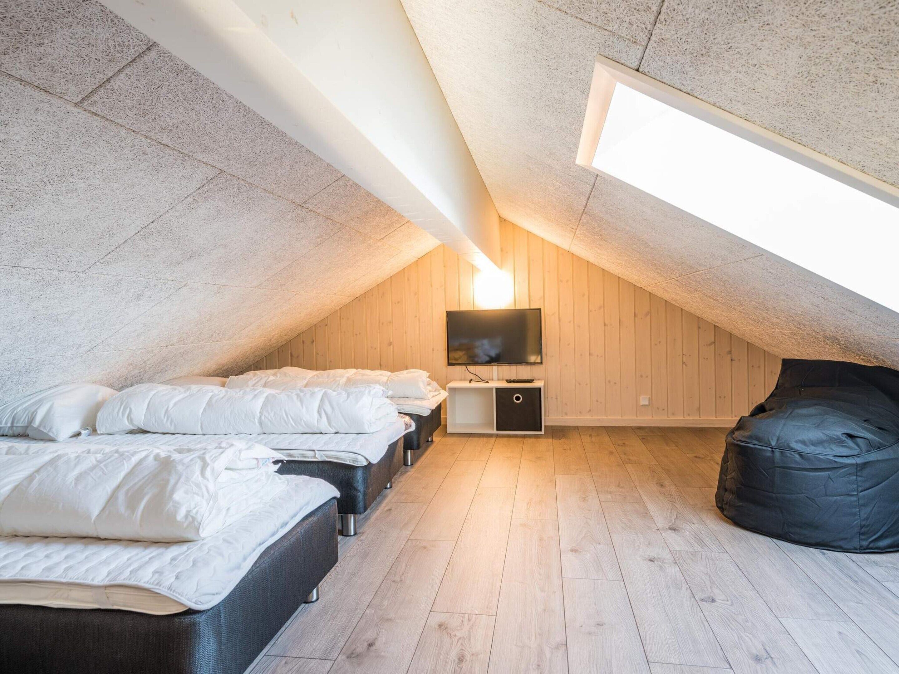 A cozy attic bedroom with a sloped ceiling, a flat-screen TV mounted on the wall, and a bean bag chair.