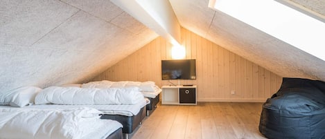 A cozy attic bedroom with a sloped ceiling, a flat-screen TV mounted on the wall, and a bean bag chair.