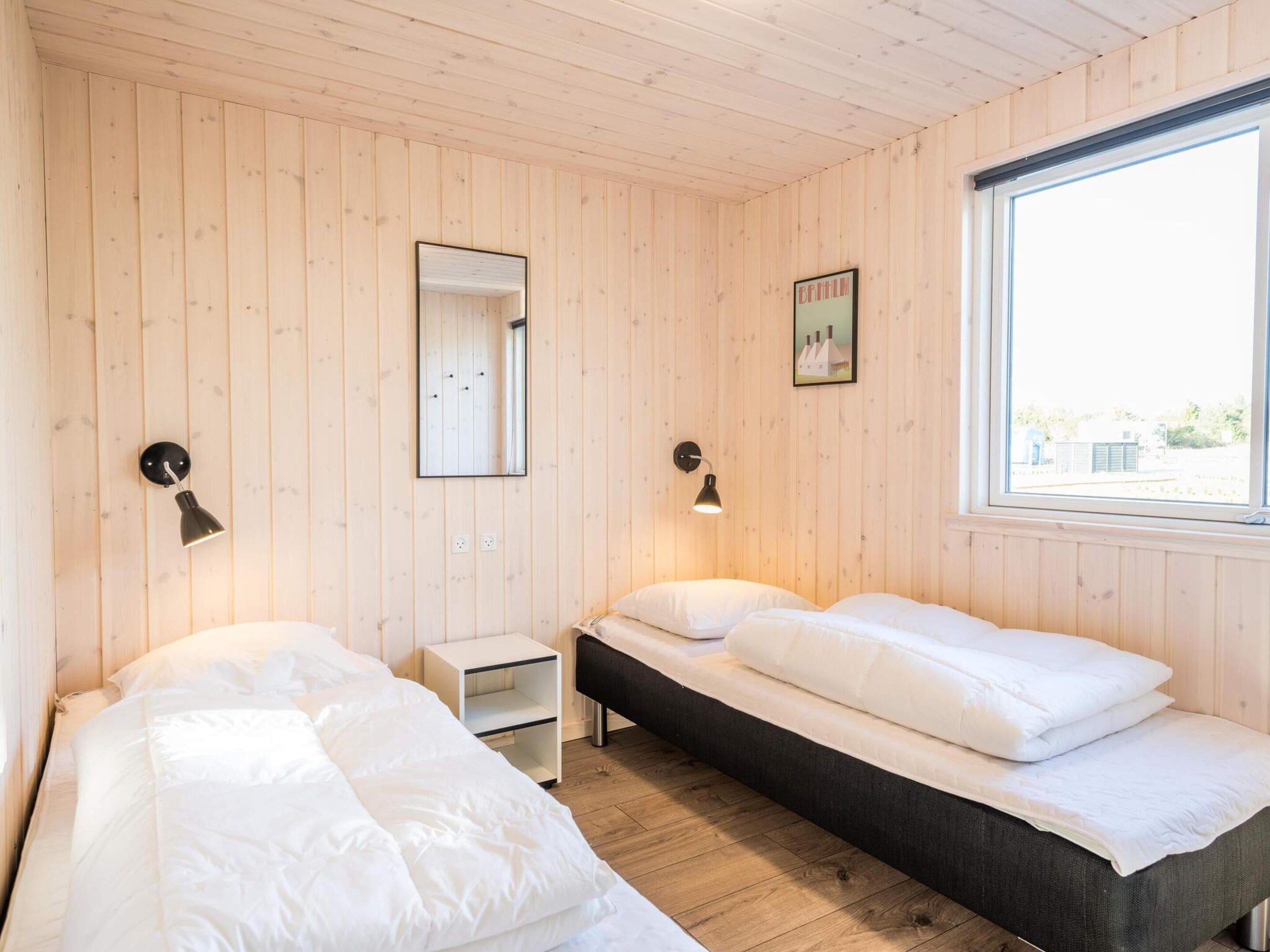 A room with two beds, a small bedside table, a mirror, and a window.