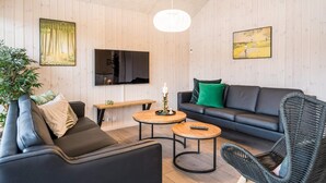 A modern living room with a sofa, two round tables, a television, and a hanging light fixture. - 5 Star Holiday Home in Norre Nebel (Norre Nebel)