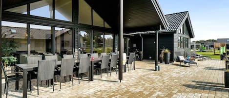 An outdoor patio area with tables and chairs, a covered seating area, and a view of a building with a tiled roof.