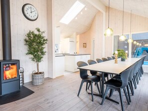 A modern kitchen with a dining area, wooden walls, a clock, and a fireplace. - 5 Star Holiday Home in Norre Nebel (Norre Nebel)