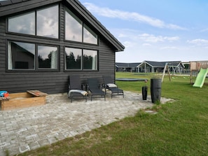Relax on the patio with a view of the playground, featuring a brick floor, lounge chairs, and a wooden bench.