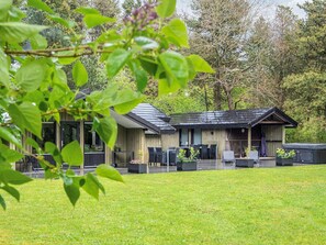 A lodge with a covered outdoor seating area, a small deck, and a grassy lawn. - 4 Star Holiday Home in Norre Nebel (Norre Nebel)
