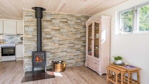 A cozy room with a stone wall, a wood-burning stove, a wooden cabinet, and a window with a view of trees. - Holiday Home in Tarm (Tarm)